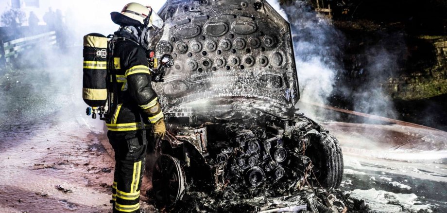 Feuerwehrmann steht vor verbranntem Pkw
