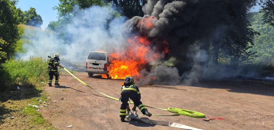 Brennendes Auto. Viel Rauch und Feuerwehrangehörige die löschen